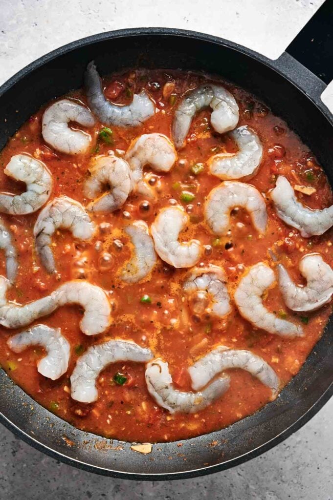Shrimp cooking in a skillet with a rich, red tomato-based sauce and herbs, perfectly reminiscent of classic shrimp and grits.
