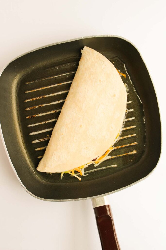 A folded quesadilla cooking in a square pan on a stovetop.