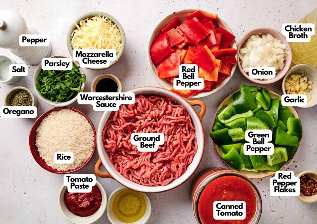 Various labeled ingredients for Air Fryer Stuffed Pepper Casserole are arranged on a countertop, including ground beef, rice, bell peppers, onion, garlic, cheese, tomato products, herbs, and seasonings.