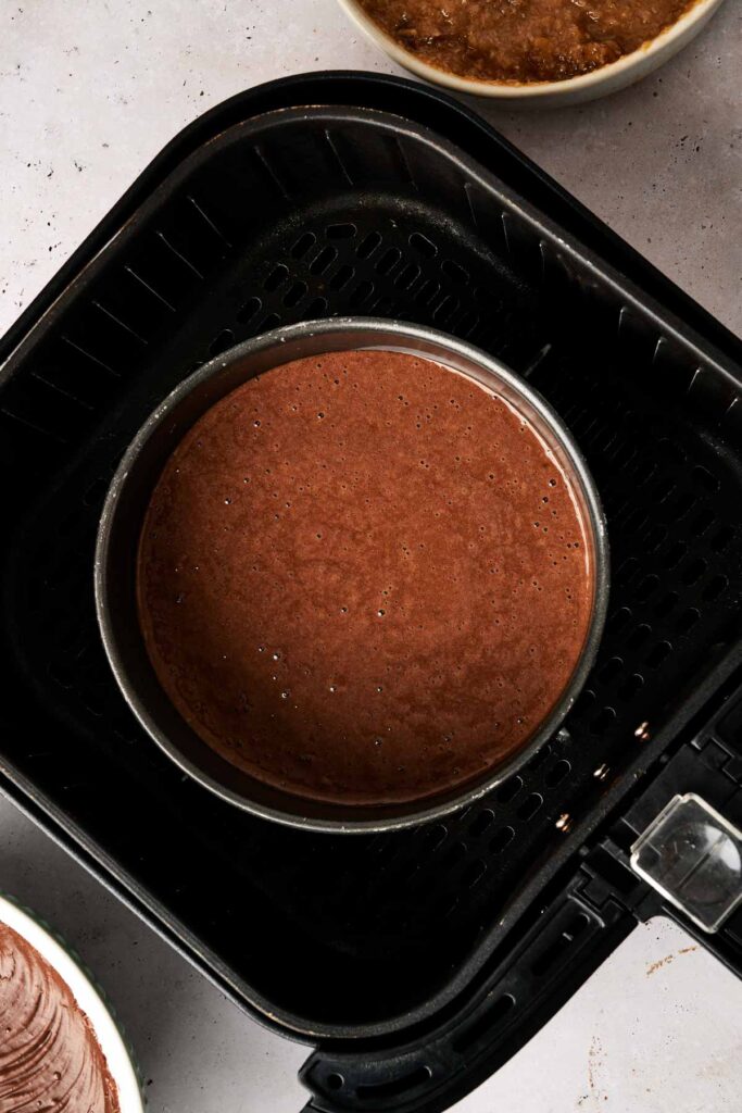 A luscious air fryer German chocolate cake batter sits in a round pan, surrounded by bowls, ready to transform into a delightful dessert.