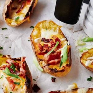 Air Fryer Loaded Potato Skins, topped with melted cheese, crispy bacon, and chopped green onions on parchment paper.