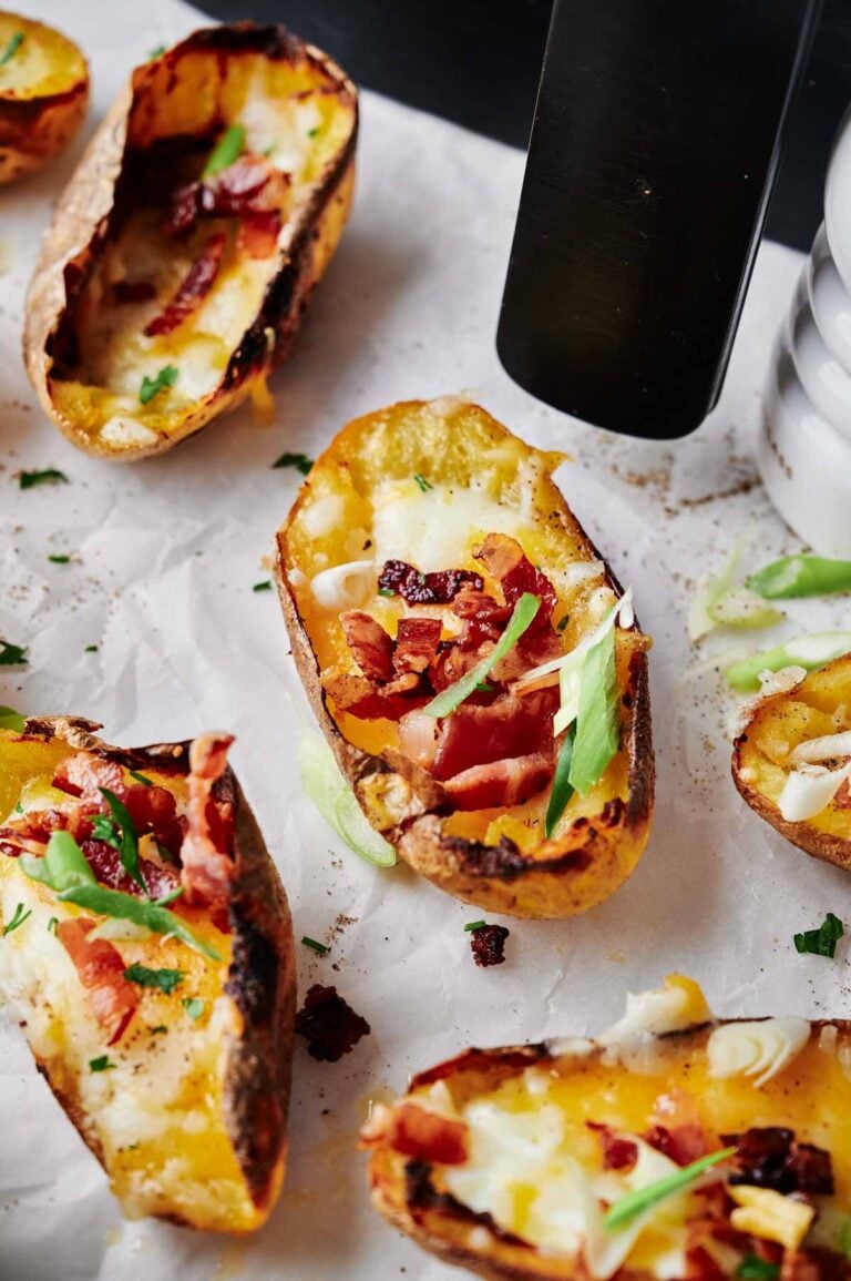 Air Fryer Loaded Potato Skins, topped with melted cheese, crispy bacon, and chopped green onions on parchment paper.