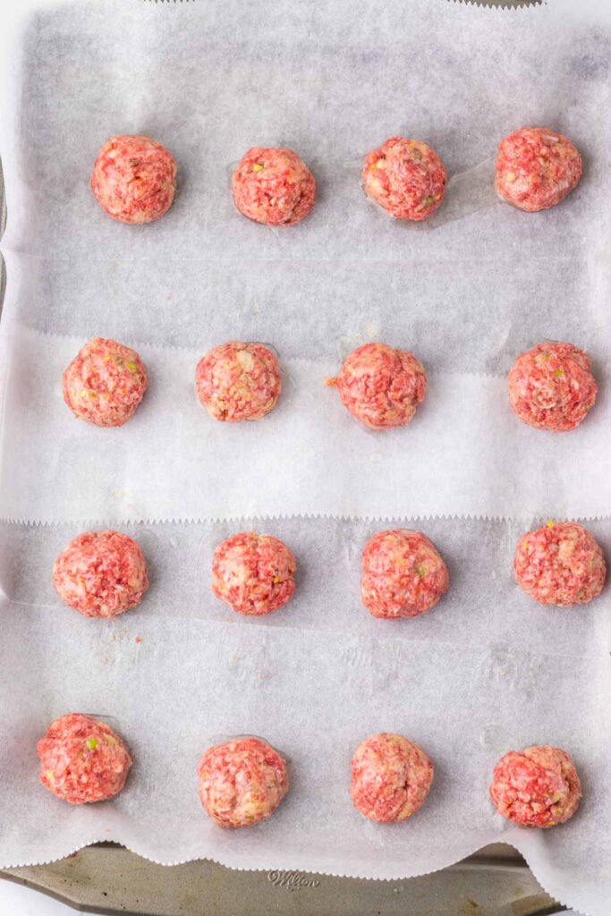 Firecracker meatballs are arranged evenly on a parchment-lined baking sheet, ready to ignite your taste buds.