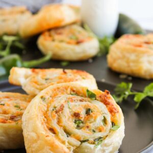 Close-up of jalapeno popper pinwheels, beautifully spiraled with cheese and herbs, resting on a dark plate and garnished with fresh cilantro.