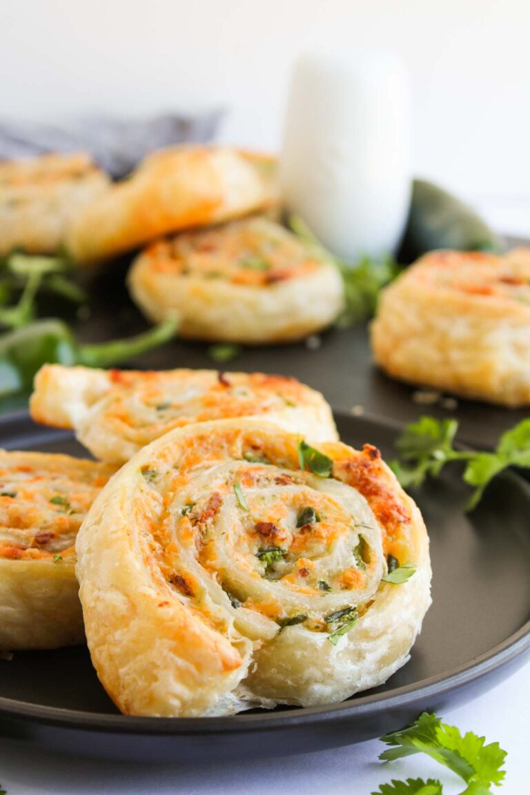 Close-up of jalapeno popper pinwheels, beautifully spiraled with cheese and herbs, resting on a dark plate and garnished with fresh cilantro.