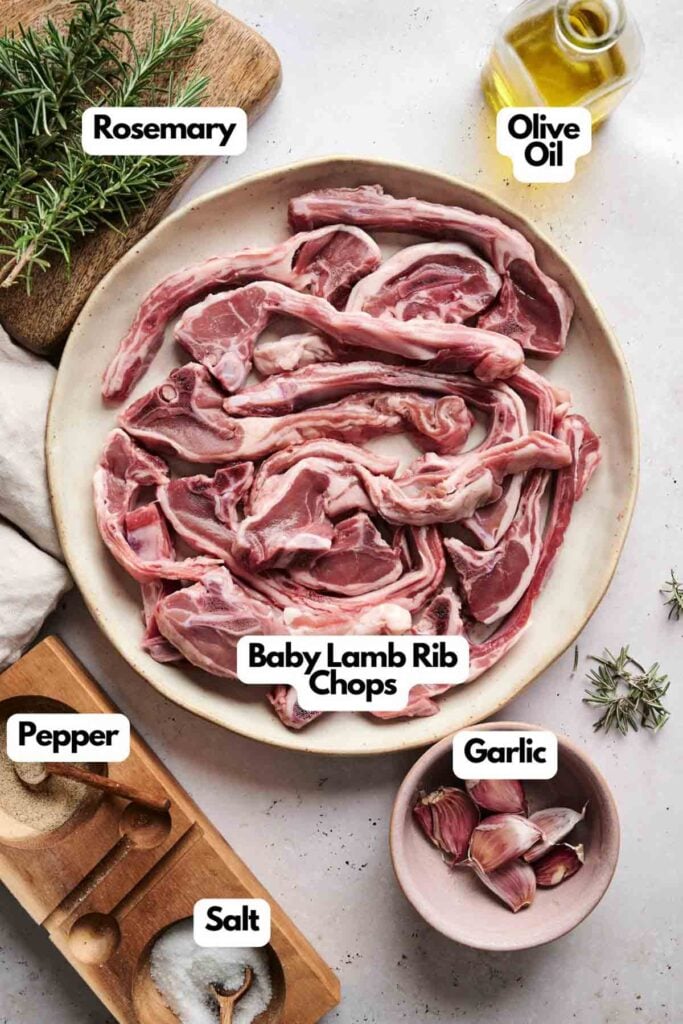 A plate of raw lamb chops, adorned with fresh rosemary, garlic, and a drizzle of olive oil, is perfectly seasoned with salt and pepper on a light surface.