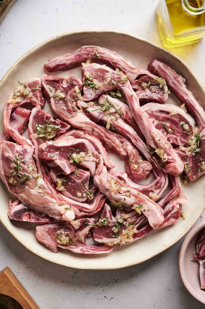 A plate of raw, marinated lamb chops brimming with garlic and herbs sits invitingly on the table. A bottle of olive oil peeks from the corner, ready to join in the culinary magic.
