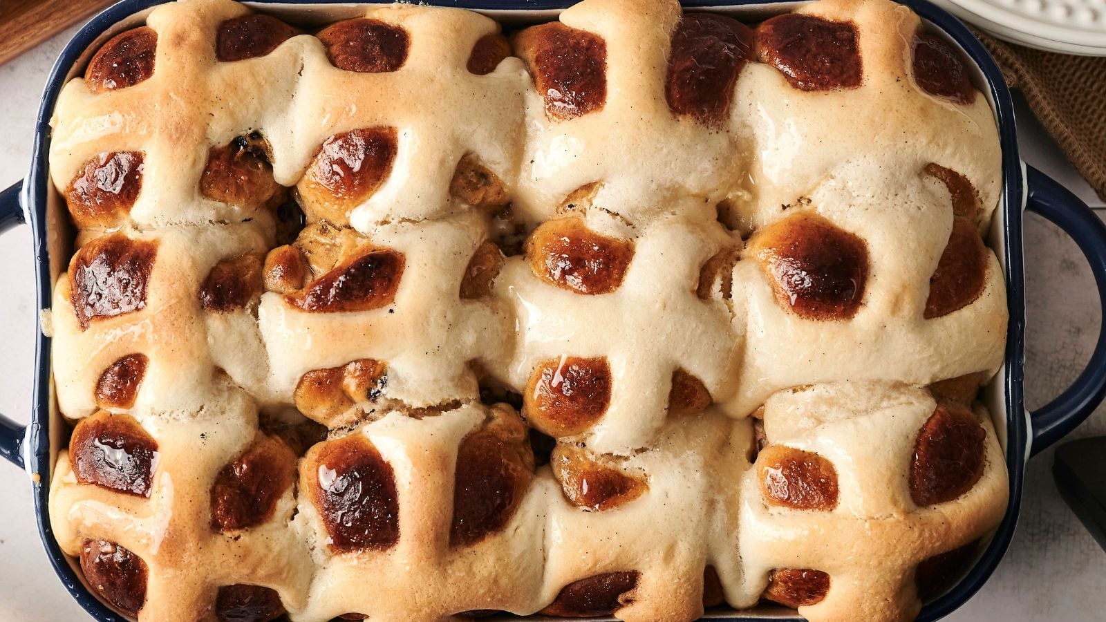 A baking dish filled with freshly baked hot cross buns, featuring a golden-brown crust and white icing crosses on top.