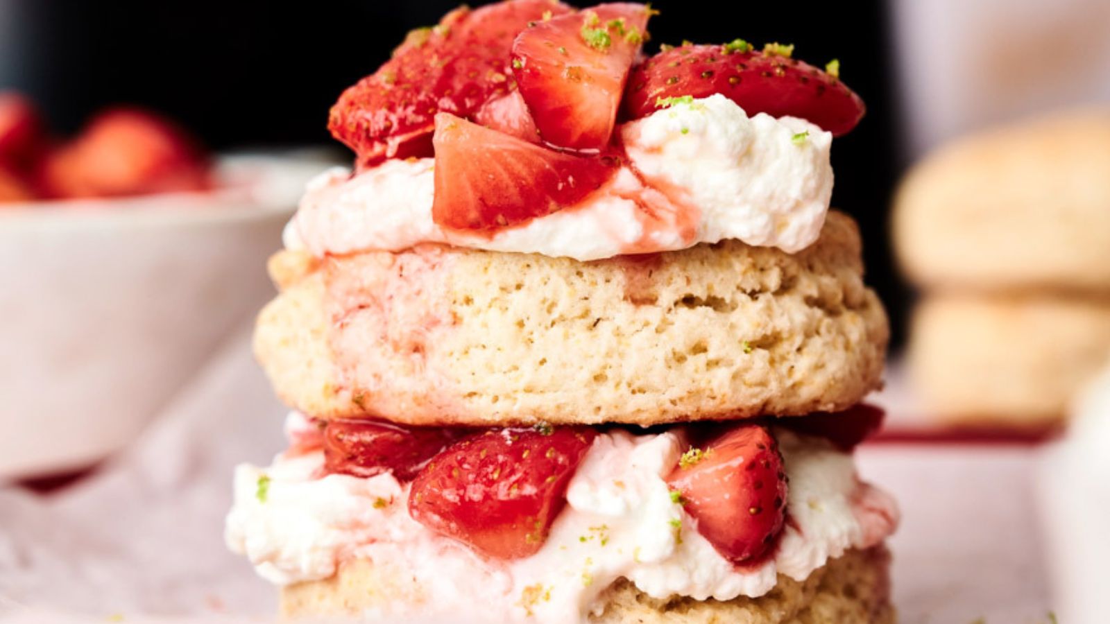 Two layers of biscuit with cream and sliced strawberries in between, topped with more strawberries and a sprinkle of green zest.