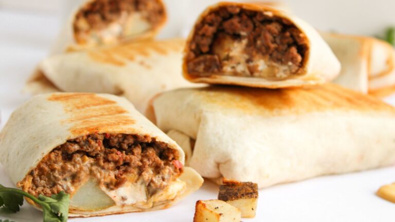 Close-up of several cut and whole burritos filled with seasoned ground beef and melted cheese, placed on a white surface.