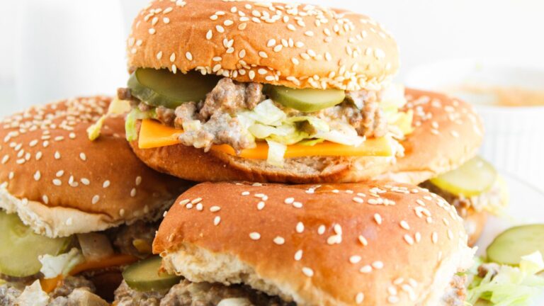 Three sesame seed burgers stacked, topped with lettuce, cheese, pickles, and a meaty filling.