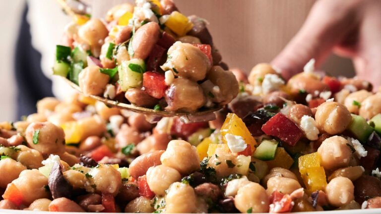 Spoon serving a colorful chickpea salad with chopped cucumbers, bell peppers, red onion, and feta cheese.