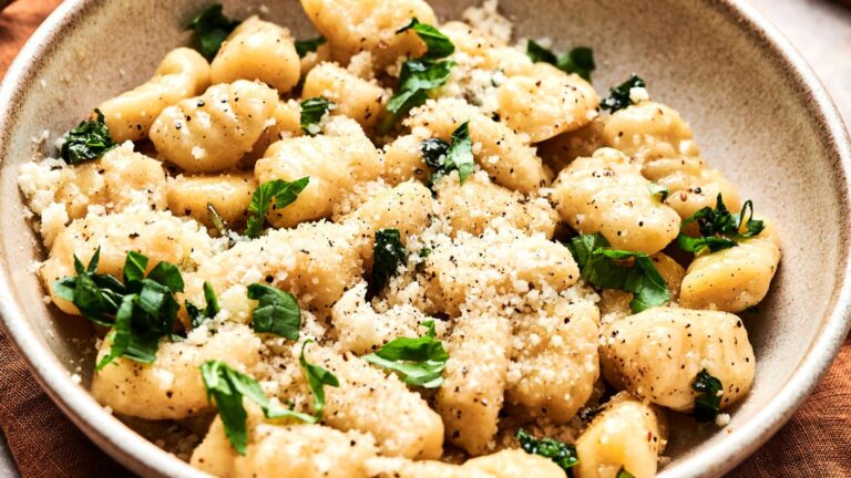 A bowl of gnocchi sprinkled with grated cheese, black pepper, and garnished with fresh basil leaves.