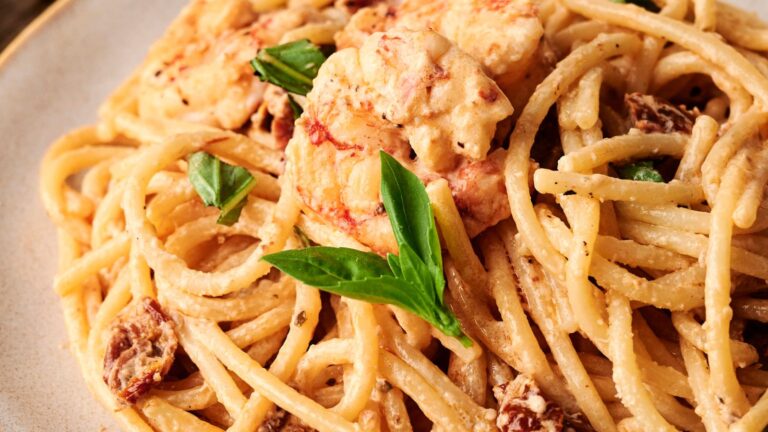 A plate of spaghetti with creamy sauce, shrimp, sun-dried tomatoes, and basil leaves.