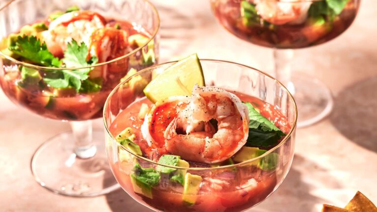 Three glass cups filled with shrimp cocktail, featuring shrimp, avocado, lime wedges, and cilantro, placed on a table.
