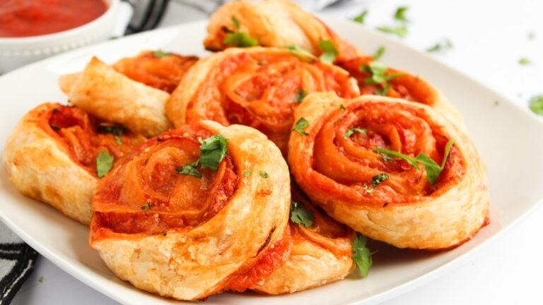 A plate of cheese and tomato puff pastry pinwheels garnished with fresh cilantro.