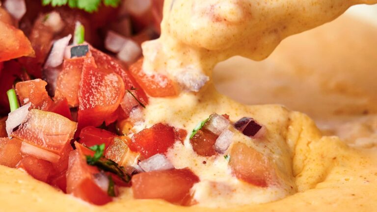 Close-up of creamy cheese dip being poured over chopped tomato salsa with diced onions and cilantro.