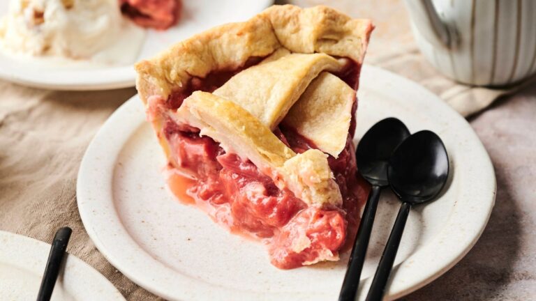 Slice of strawberry pie on a plate with two black spoons beside it.