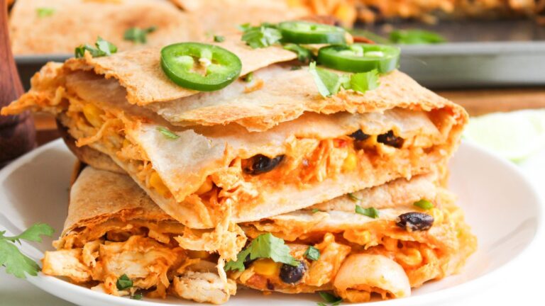 A stack of quesadilla slices filled with chicken, cheese, and black beans, topped with jalapeño slices and cilantro, on a white plate.
