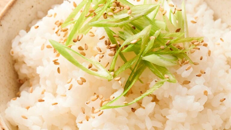 A bowl of white rice topped with sliced green onions and sprinkled with sesame seeds.