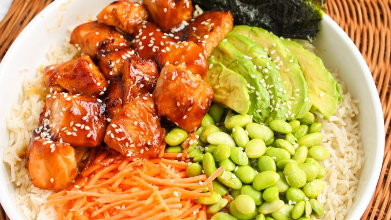 Bowl with rice, glazed chicken, sliced avocado, edamame, shredded carrots, seaweed, and sesame seeds.