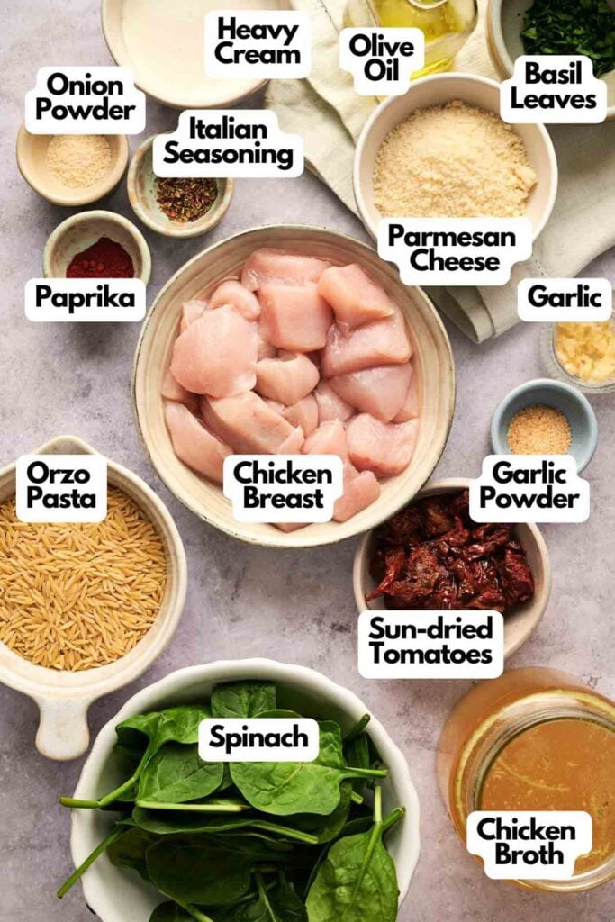 A vibrant spread of flavors awaits with Marry Me Chicken Orzo&mdash;ingredients laid out include succulent chicken breast, tender orzo pasta, fresh spinach, tangy sun-dried tomatoes, aromatic garlic, parmesan cheese, and a medley of seasonings like paprika and Italian herbs.