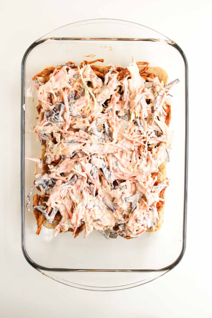 A glass baking dish containing a layer of bread topped with shredded vegetables in a creamy dressing&mdash;perfect as a flavorful side for BBQ Chicken Sliders.