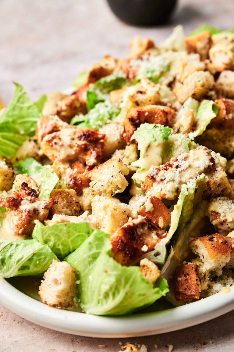 A Chicken Caesar Salad featuring tender grilled chicken, romaine lettuce, croutons, grated cheese, and creamy dressing elegantly served on a white plate.