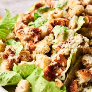 A Chicken Caesar Salad featuring tender grilled chicken, romaine lettuce, croutons, grated cheese, and creamy dressing elegantly served on a white plate.