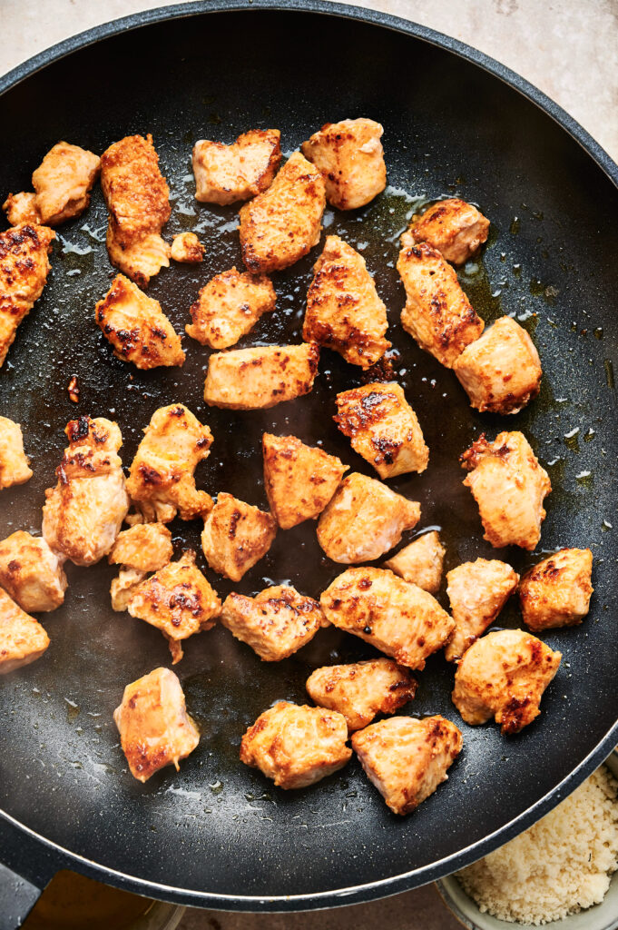 Chunks of browned chicken simmer in a black skillet, ready to elevate your Chicken Caesar Salad with savory perfection.