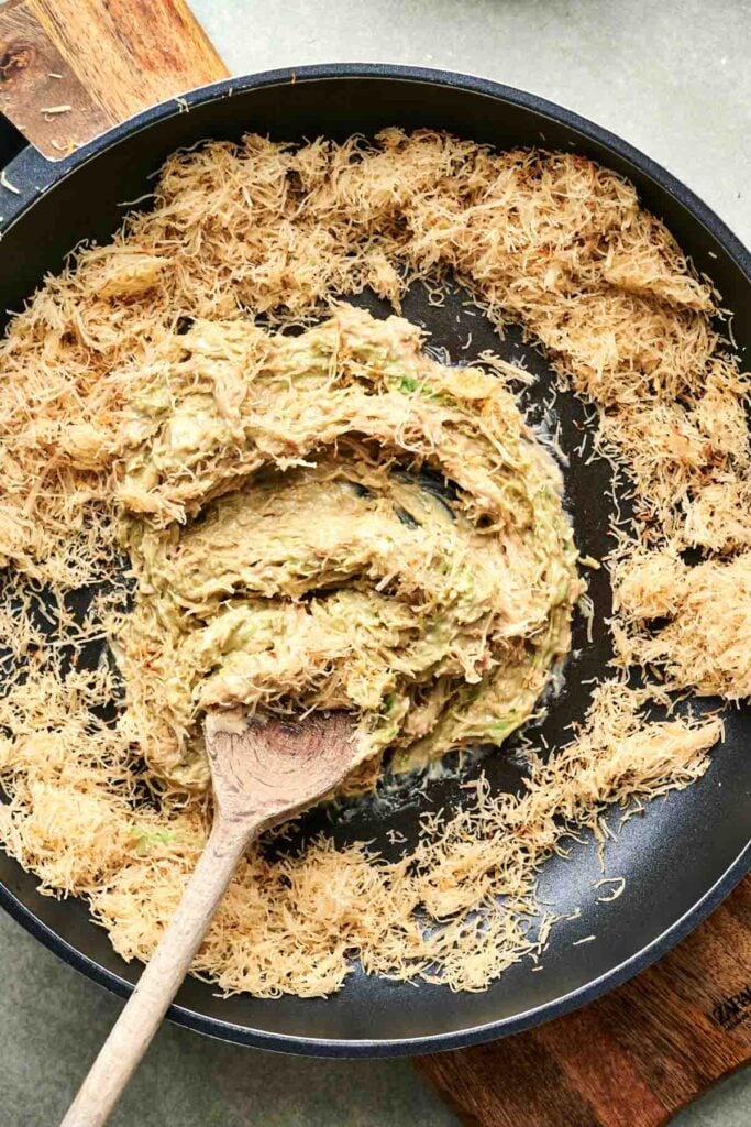 A pan with shredded pastry encircling a creamy, mixed filling, infused with a touch of Dubai chocolate and stirred with a wooden spoon.