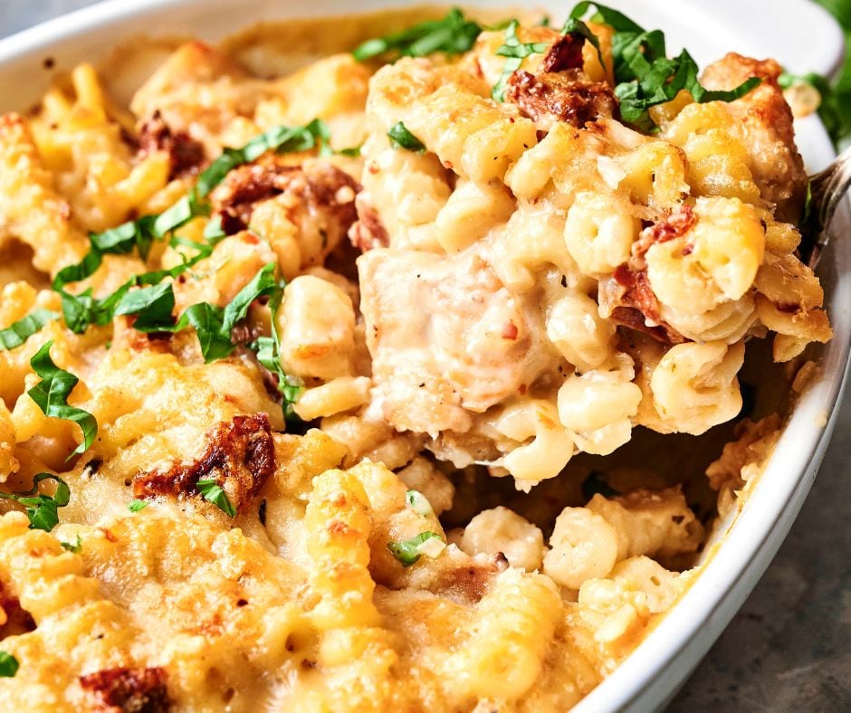 A creamy pasta bake with melted cheese, sun-dried tomatoes, and a hint of "Marry Me Chicken Casserole" allure, garnished with fresh herbs in a white dish.