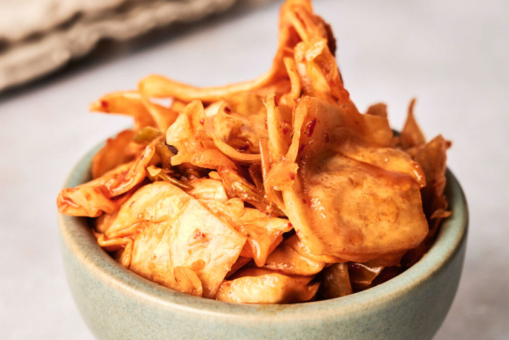 A small bowl filled with sliced, stir-fried tofu skin in a savory sauce, served alongside tangy kimchi.