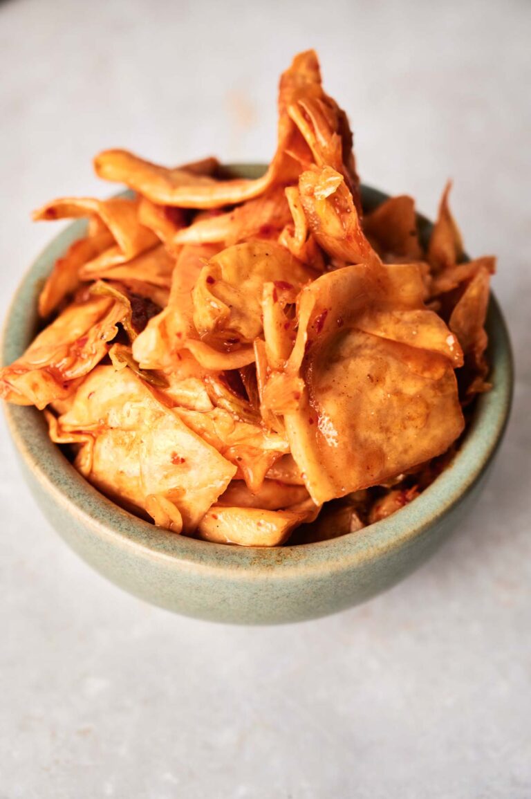 A green bowl filled with spicy, marinated kimchi cabbage slices on a light-colored surface.