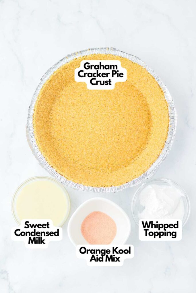 A Graham cracker pie crust sits on a marble surface, surrounded by bowls of sweetened condensed milk, vibrant orange Kool-Aid mix, and fluffy whipped topping—everything you need to create a delightful Kool Aid Pie.