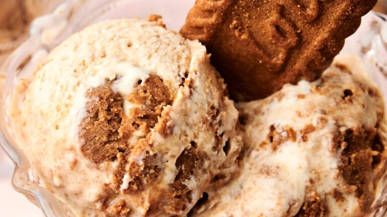 A close-up of two scoops of ice cream with chunks of cookie, topped with a whole cookie in a glass bowl.