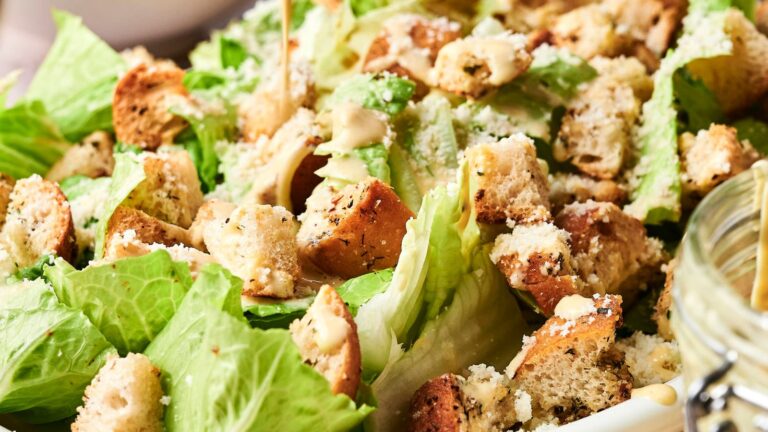 Close-up of Caesar salad with romaine lettuce, seasoned croutons, and grated cheese, drizzled with dressing.