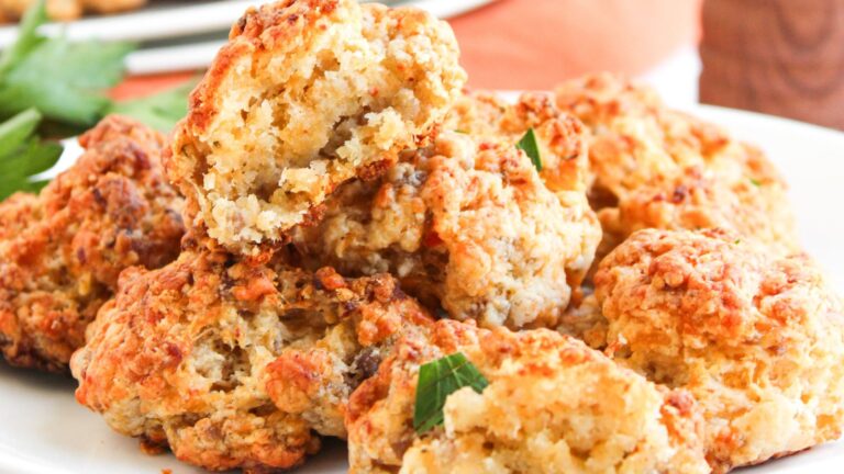 A plate of golden-brown biscuits stacked with a parsley garnish, one biscuit broken to reveal a soft, crumbly interior.