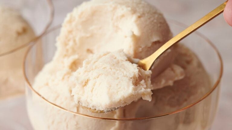 A close-up of a spoon scooping vanilla ice cream from a glass bowl.