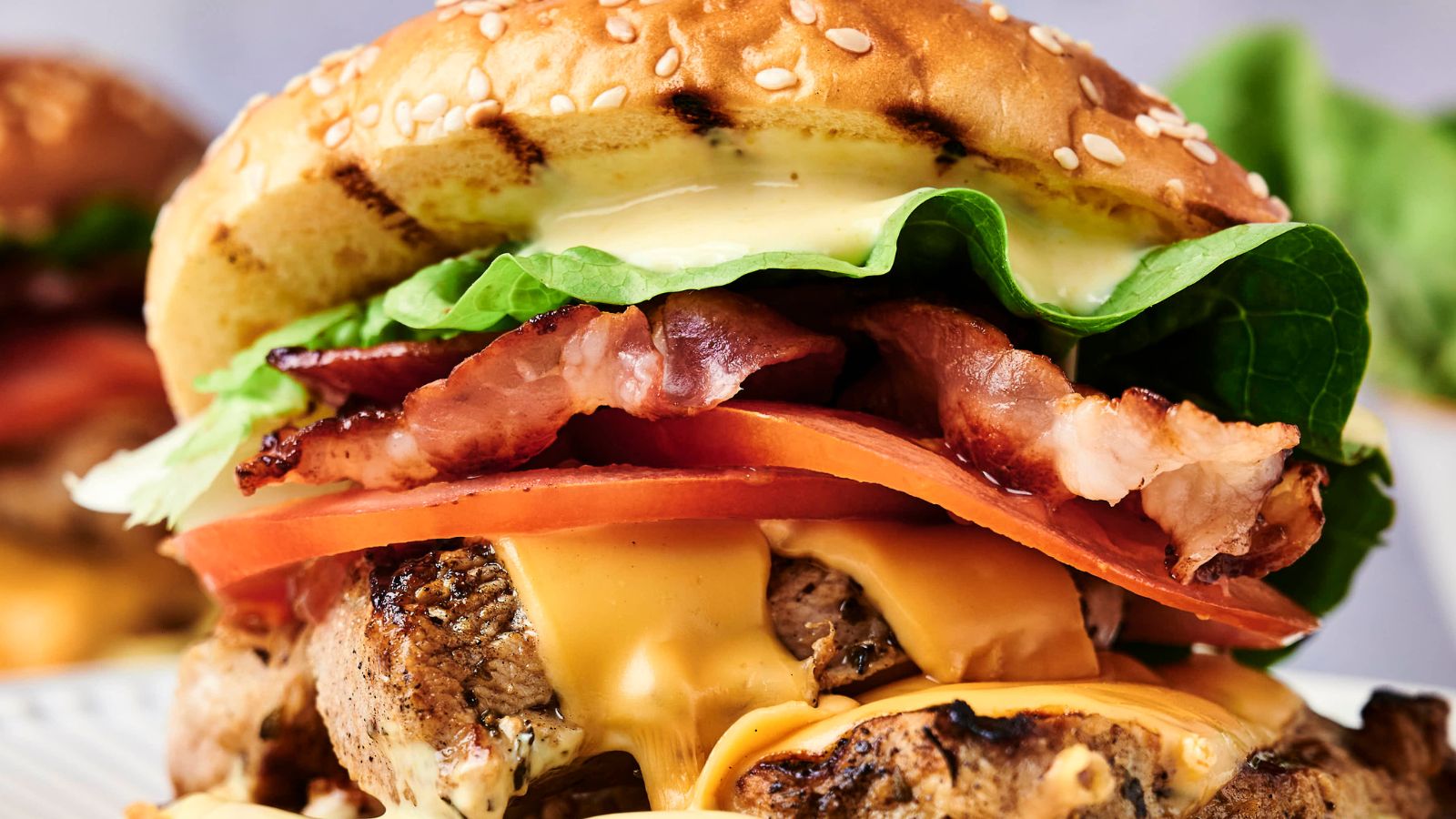 Close-up of a cheeseburger with a sesame bun, bacon, lettuce, tomato, cheese, and beef patty.