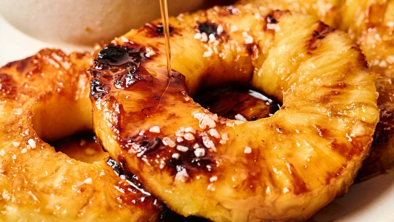 Close-up of grilled pineapple rings topped with coarse salt and drizzled with syrup.