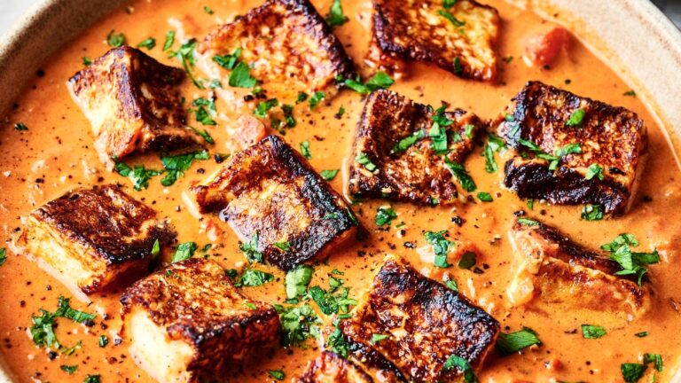 A dish of grilled paneer cubes in a creamy tomato sauce, garnished with chopped cilantro.