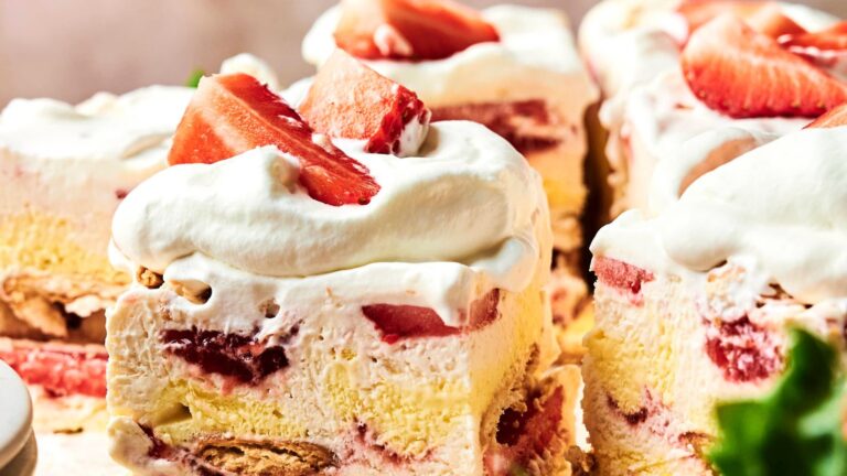 Close-up of strawberry shortcake squares topped with whipped cream and sliced strawberries, showing layers of cream, strawberries, and cake.