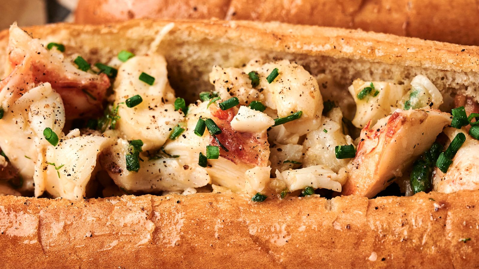 A close-up of a sandwich roll filled with chunks of seasoned lobster meat, garnished with chopped chives.