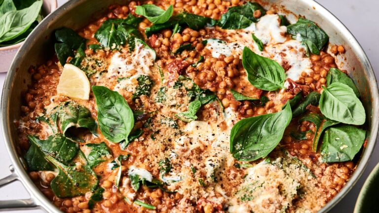 A pan of chickpeas, greens, and tomato sauce topped with fresh basil, lemon wedge, and melted cheese.