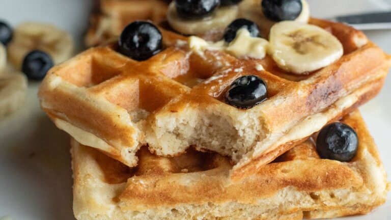 Two waffles topped with banana slices, blueberries, and a pat of butter; one waffle has a bite taken out of it.