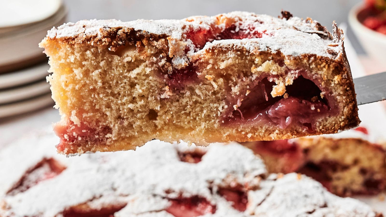 Close-up of a slice of strawberry cake dusted with powdered sugar, showing a fluffy texture and pieces of strawberries inside.