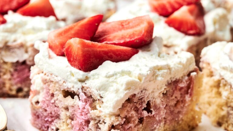 A slice of cake with a light pink and beige interior, topped with white frosting and sliced strawberries.
