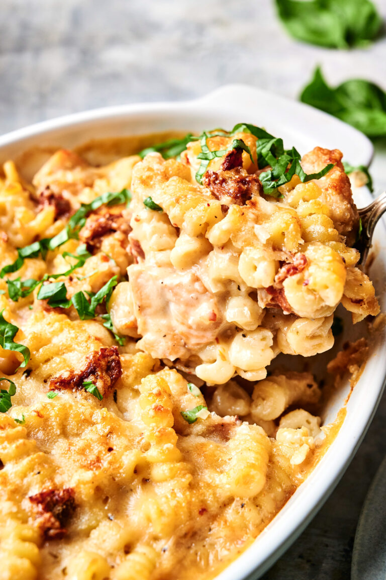 Close-up of a Marry Me Chicken Casserole featuring spiral noodles, melted cheese, tender chicken, and a sprinkle of fresh herbs in a white baking dish.