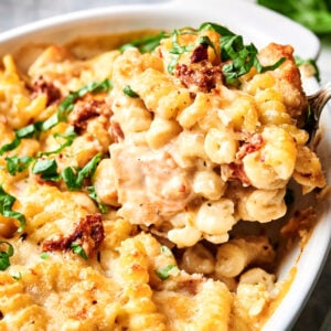 Close-up of a Marry Me Chicken Casserole featuring spiral noodles, melted cheese, tender chicken, and a sprinkle of fresh herbs in a white baking dish.